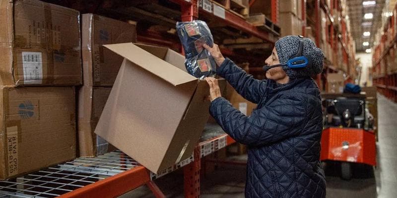 Woman putting objects inside a box, in a warehouse setting.