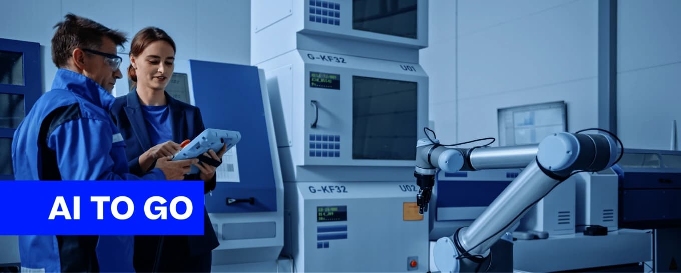 Zwei Personen stehen neben einer Maschine mit der Aufschrift „AI to Go“ und präsentieren Technologie in einem modernen Umfeld.