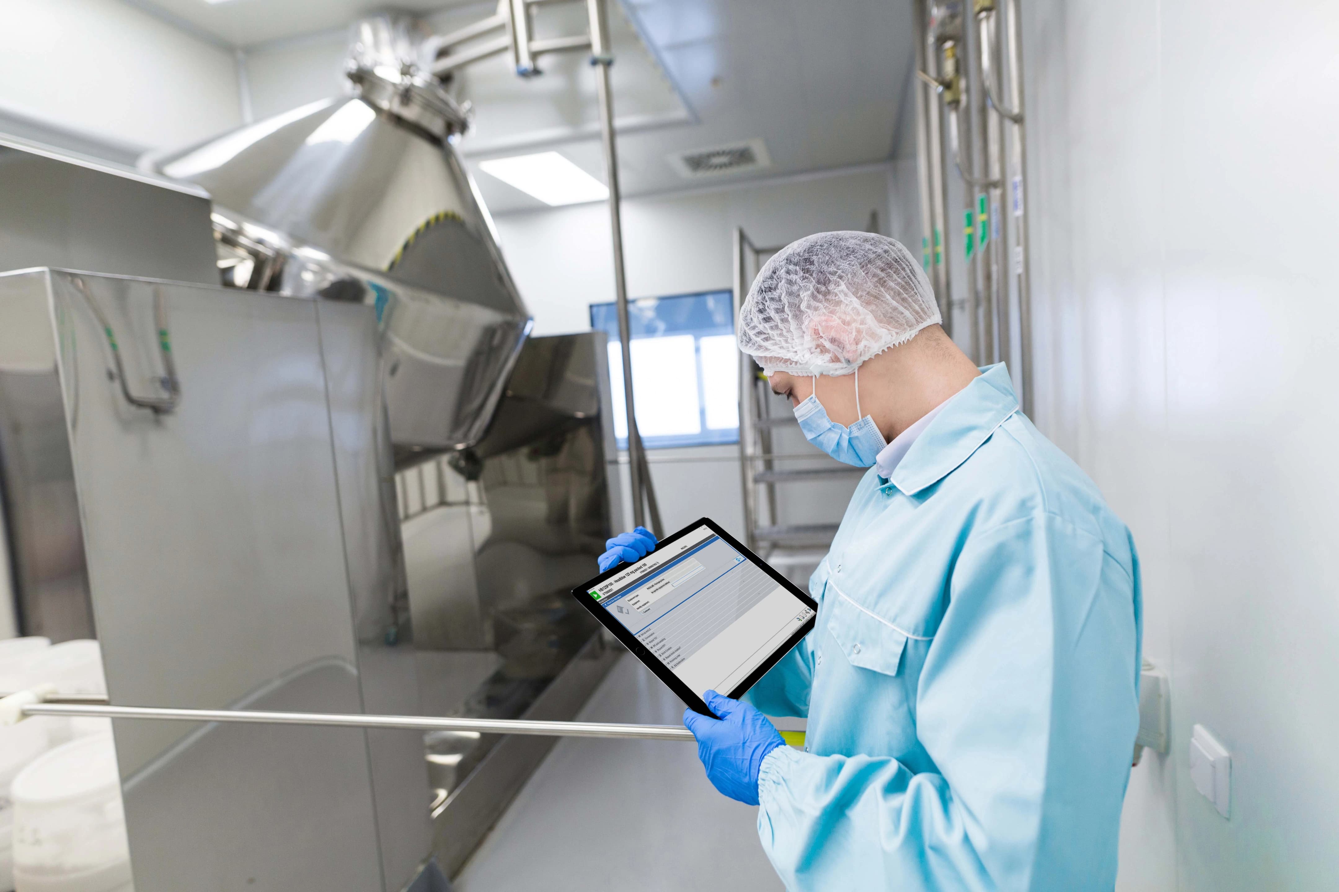 A man wearing a blue coat interacts with a tablet, demonstrating PAS-X MES software for the pharmaceutical industry.