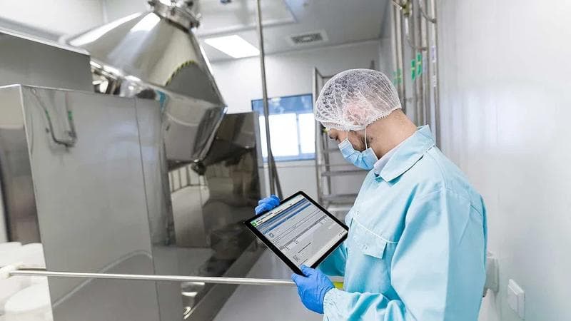 Worker holding a tablet in a pharma manufacturing place.