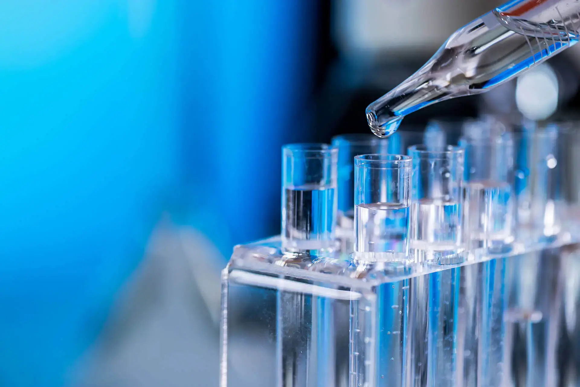 A person pours a clear liquid into a test tube, demonstrating a laboratory experiment or scientific procedure.