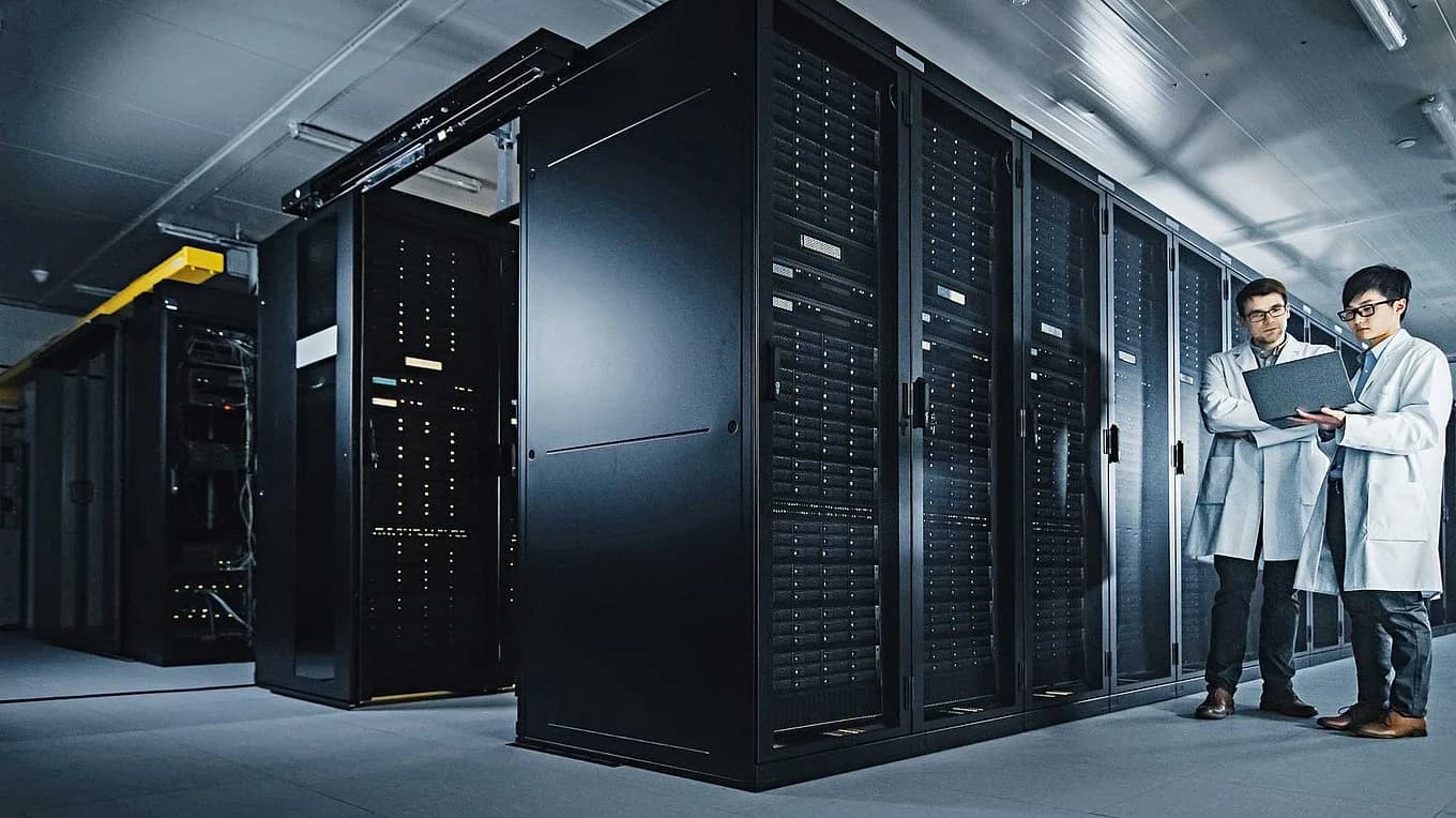 Two people in lab coats stand in front of a server