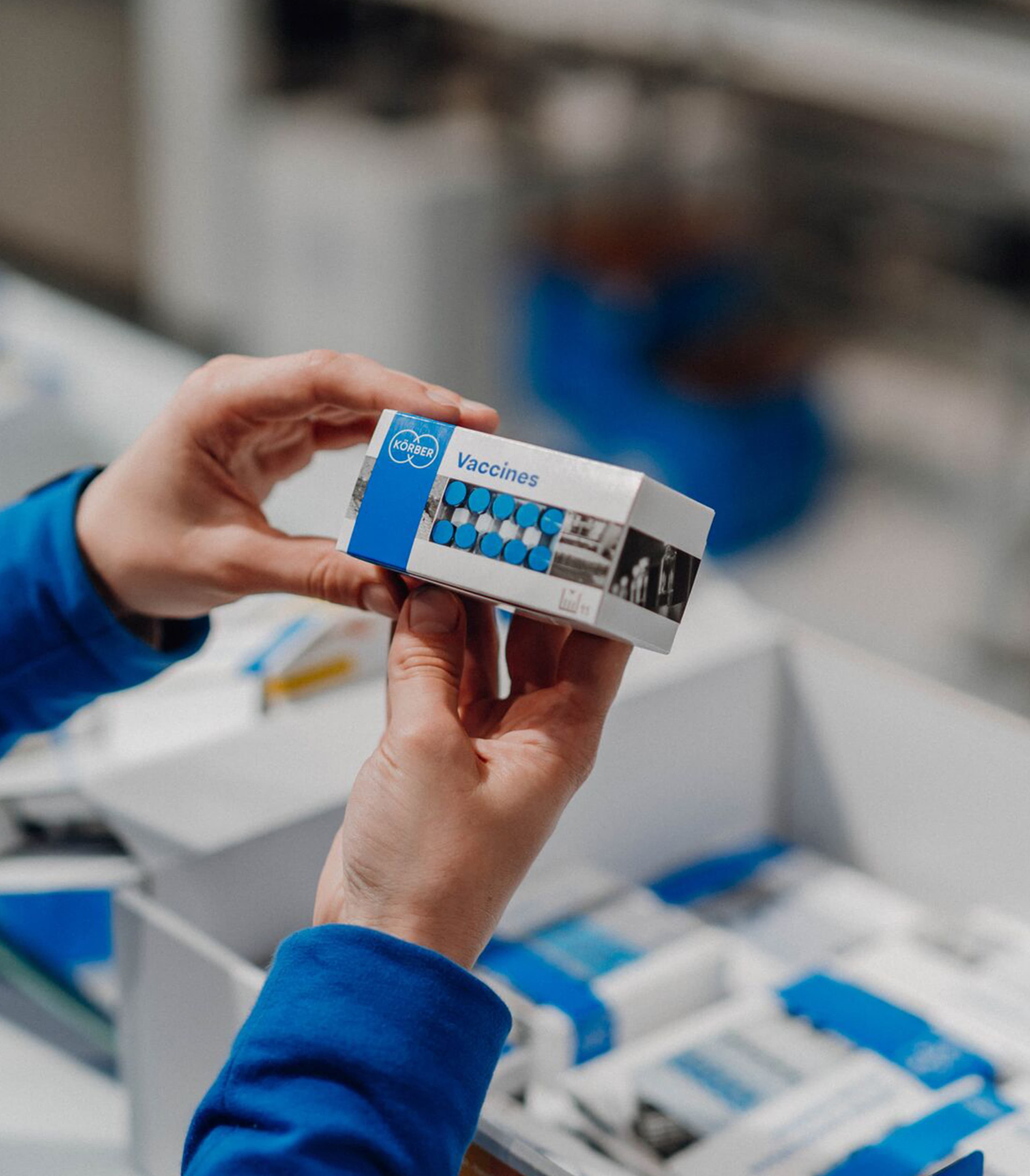 Hände halten eine Körber-Impfschachtel in einer pharmazeutischen Produktionsanlage.