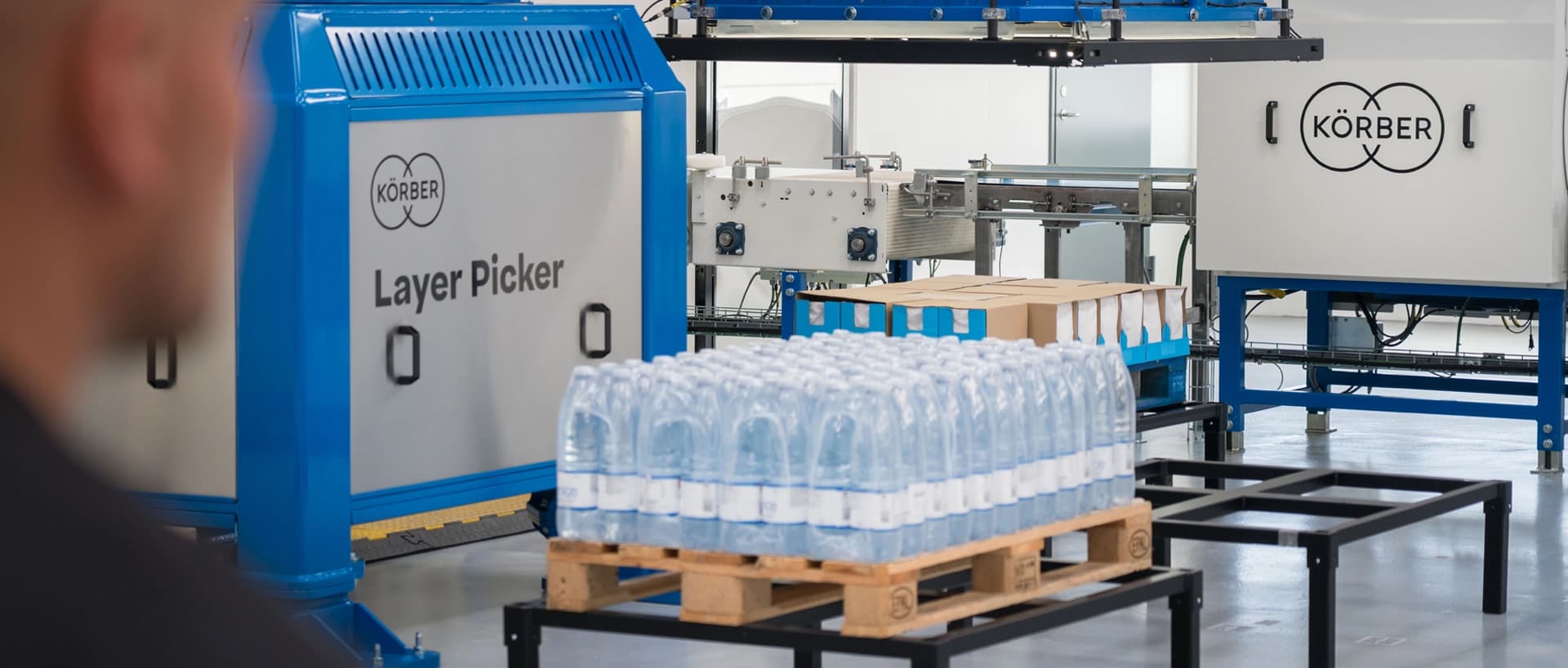 Ein Mann steht an der Lagenpickertechnik von Körber, die aktiv Flaschen produziert.