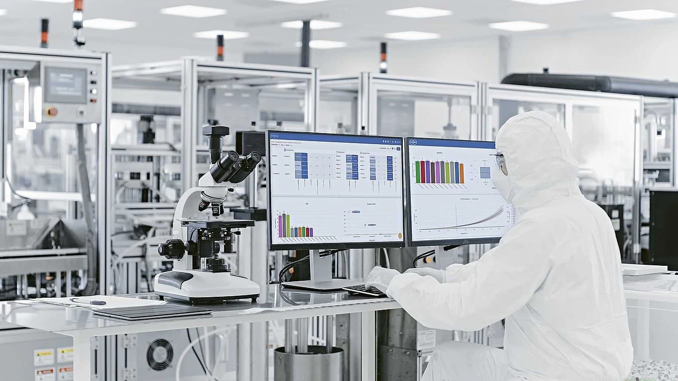 A lab-coated individual works on a computer, focusing on data analytics in the pharmaceutical industry.