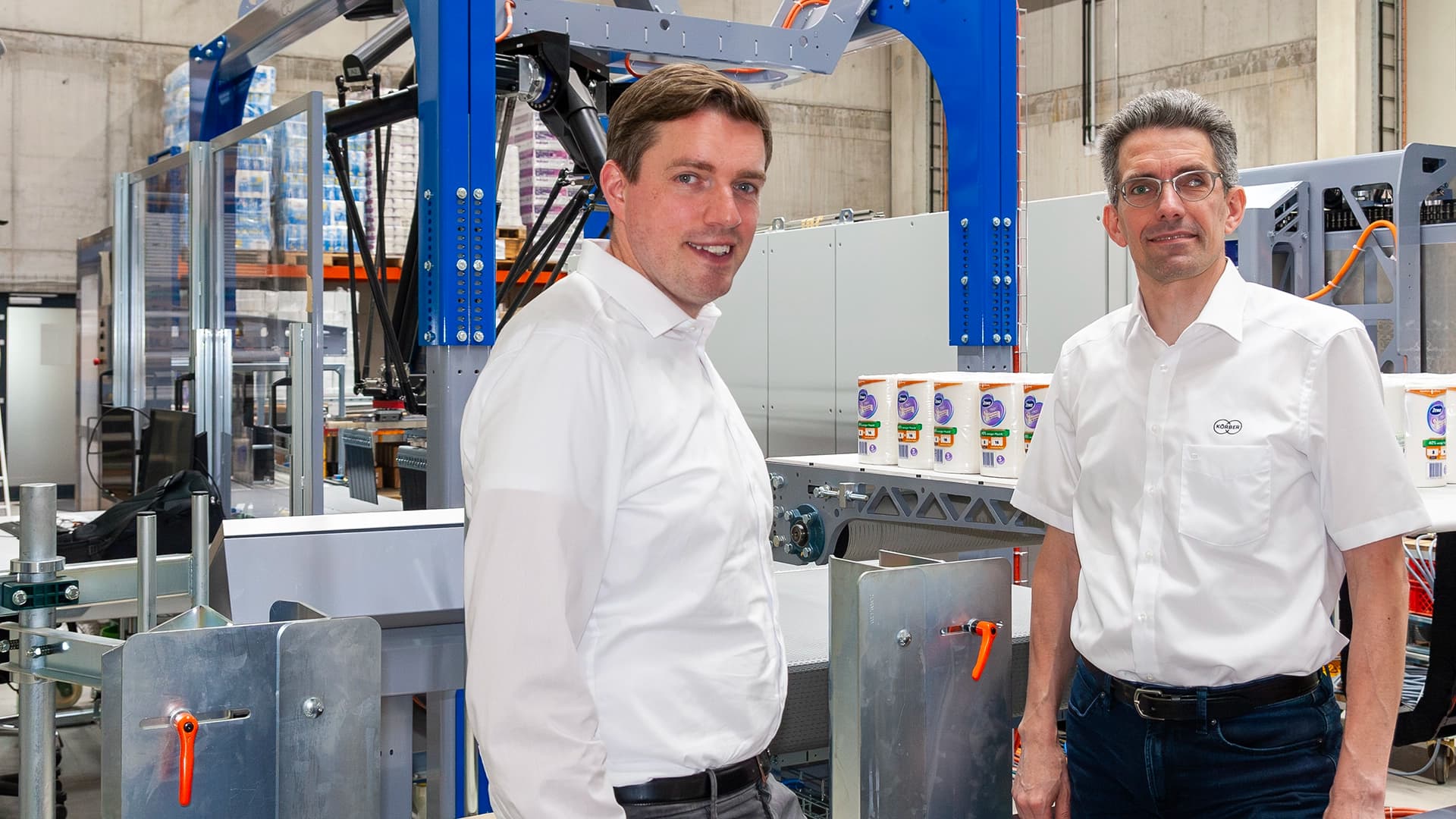 Zwei Männer stehen vor einer PA15-Lagenpalettiermaschine in einer Fabrikumgebung.
