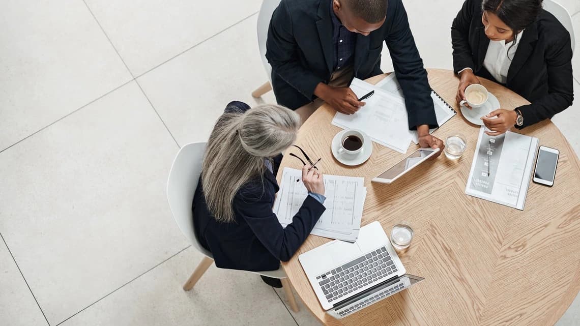 Drei Geschäftsleute an einem Tisch mit Laptops diskutieren über Audit-Daten zur Paketlogistik.