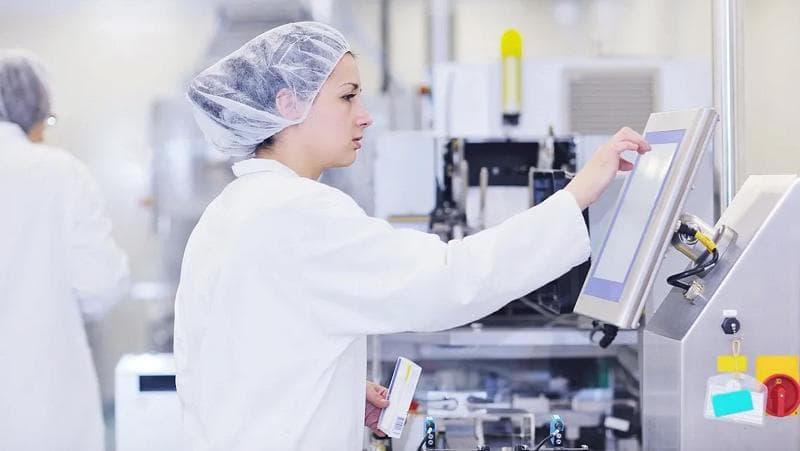 Frau in Labor-Schutzkleidung, die an Maschinen zur Arzneimittelherstellung arbeitet.