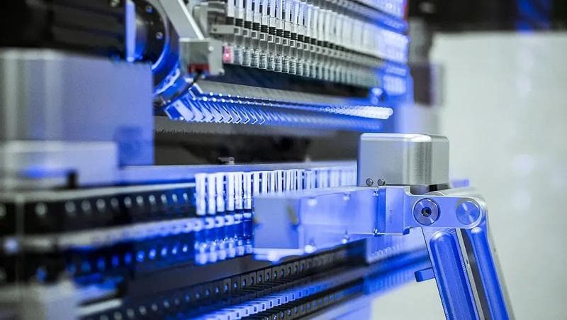 Nahaufnahme einer Maschine mit blauen Lichtern, die Teil des automatischen Spritzenhandlingsystems von Körber Pharma ist.