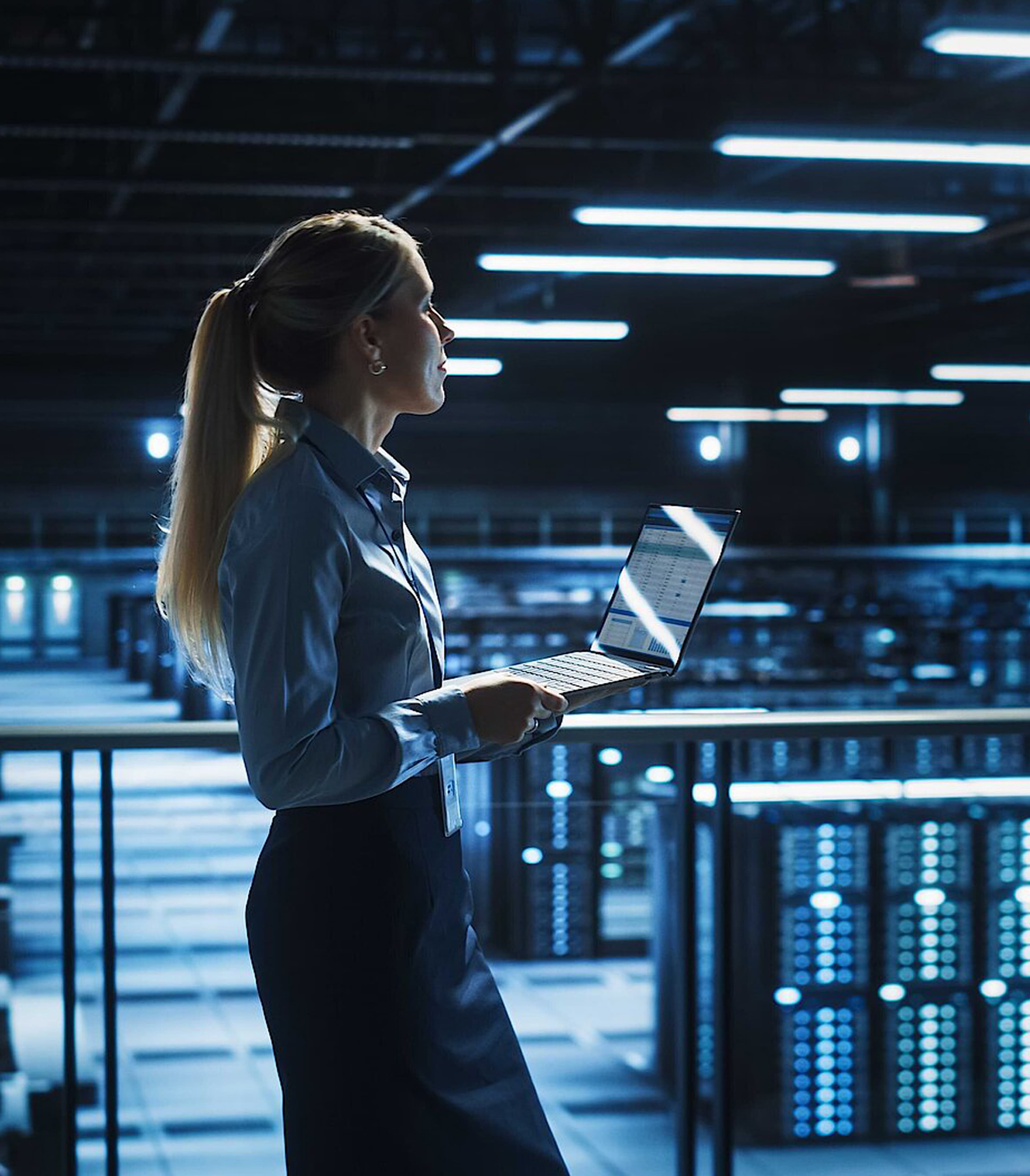 Women holding a laptop standing in a dimly lit server room