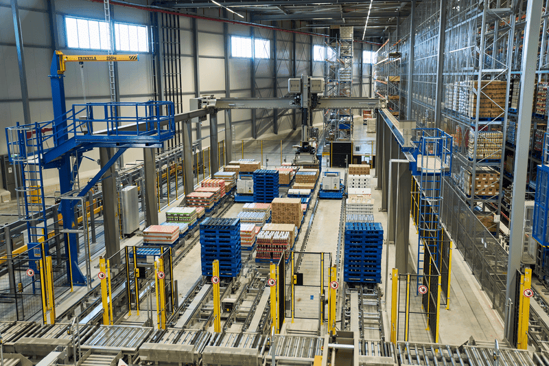 A large warehouse featuring numerous shelves lined with boxes and additional boxes on the floor.