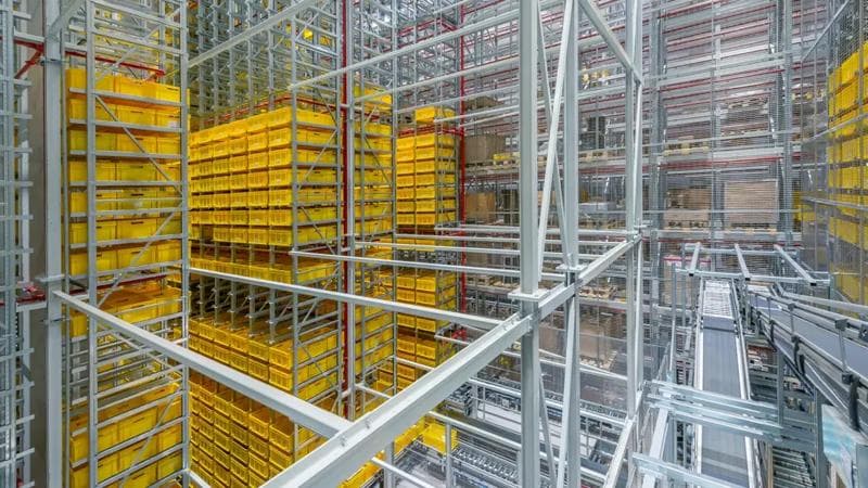 Photo from the inside of a big warehouse with metal stands and yellow containers.