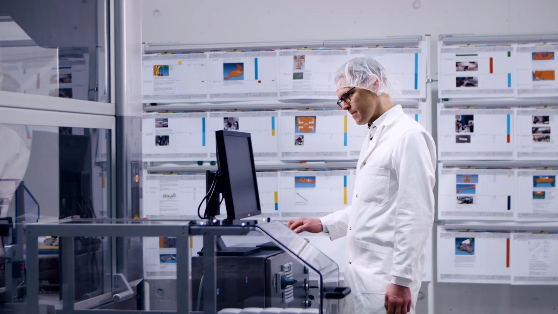 A man in a lab coat is focused on working at a computer in a laboratory setting
