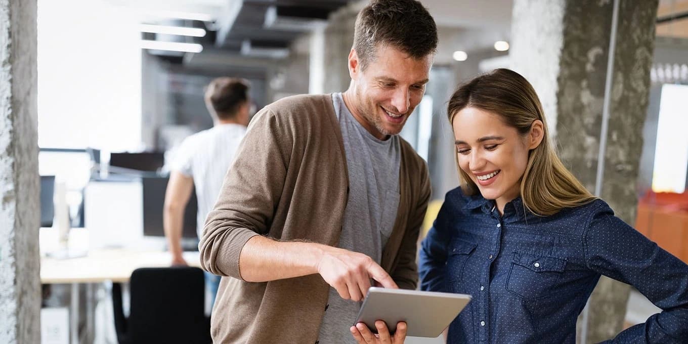A man and woman are engaged in discussion while looking at a tablet together.