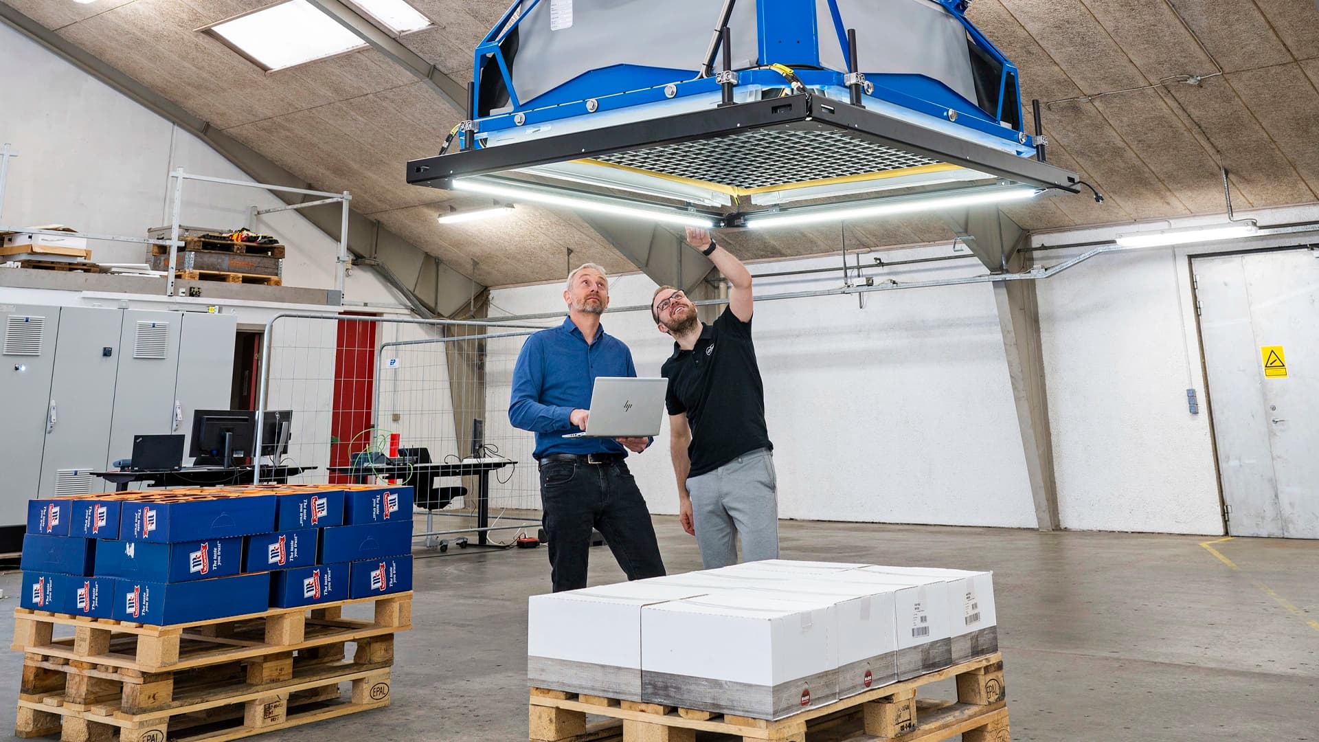 Two Körber employees looking to a Siemens warehouse machine.