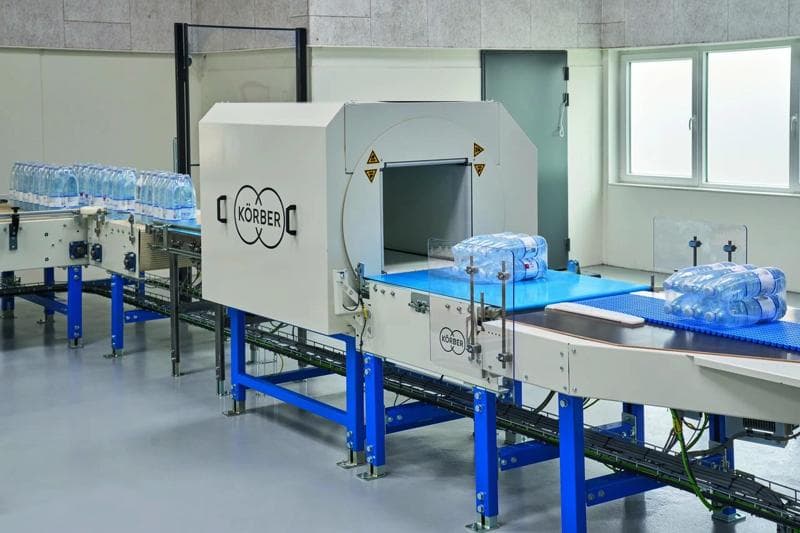 Der Lagenpalettierer PA15 von Korber stapelt aktiv Wasserflaschen für die Verpackung in einer Produktionsstätte.