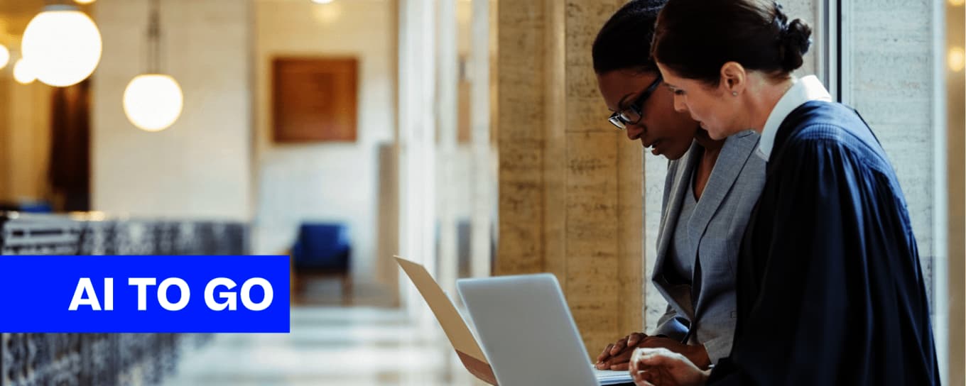 Zwei Frauen in Geschäftsanzügen arbeiten zusammen, während sie auf einen Laptop schauen.