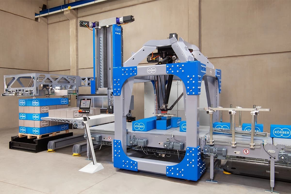 Eine Körber PA15-Lagenpalettiermaschine, die Kartons in einer Fabrikhalle zusammenstellt.