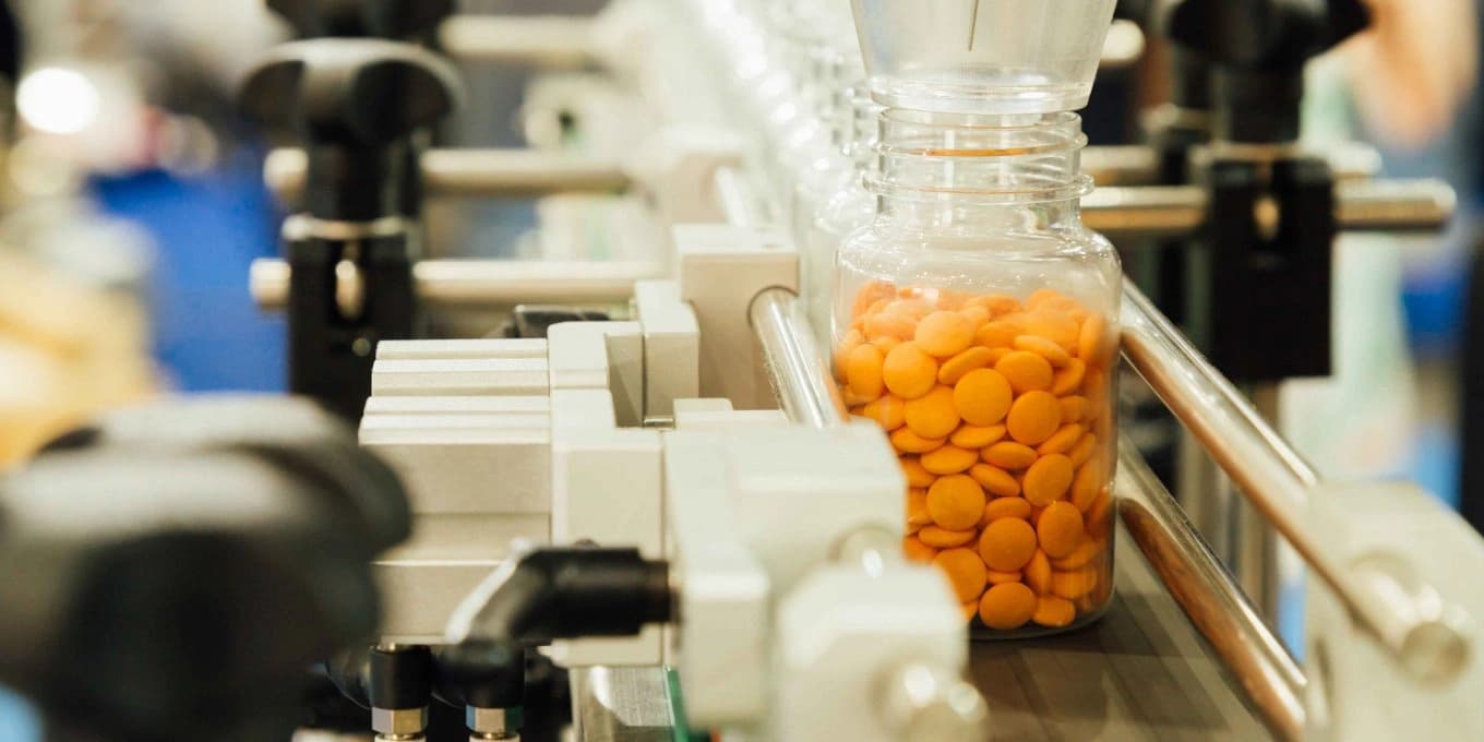 Mit Tabletten gefüllte Flaschen, die eine automatisierte pharmazeutische Verpackungslinie durchlaufen, um die regulierte Handhabung von Arzneimitteln und die Rückverfolgbarkeit zu veranschaulichen.
