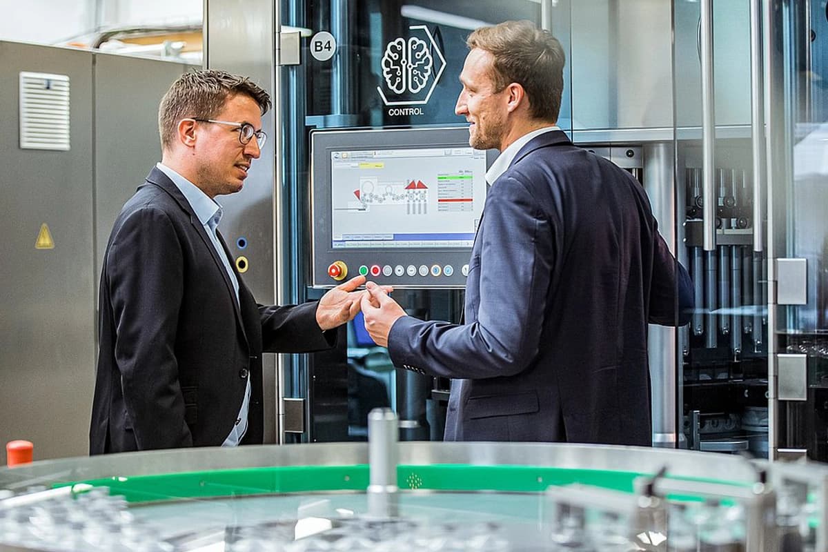 Zwei Männer in Anzügen sprechen miteinander in einer Fabrik.