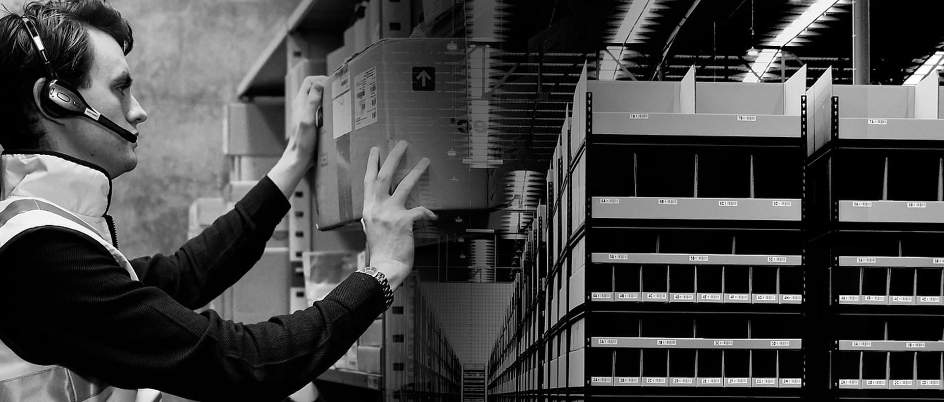 A man stands in a warehouse next to a robot, surrounded by shelves and boxes.
