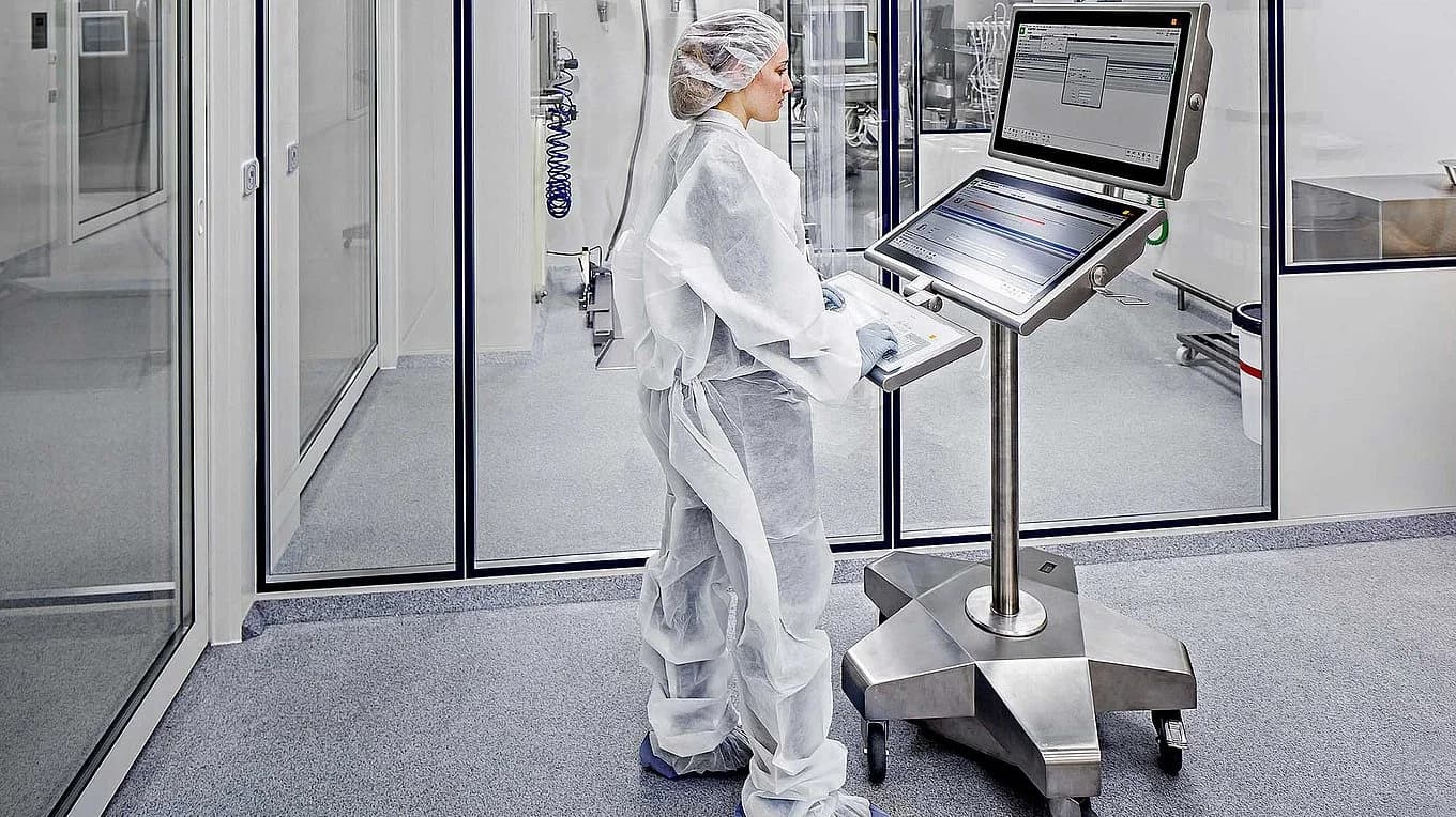 Operator in a cleanroom using a PAS-X MES workstation to manage digital production processes.