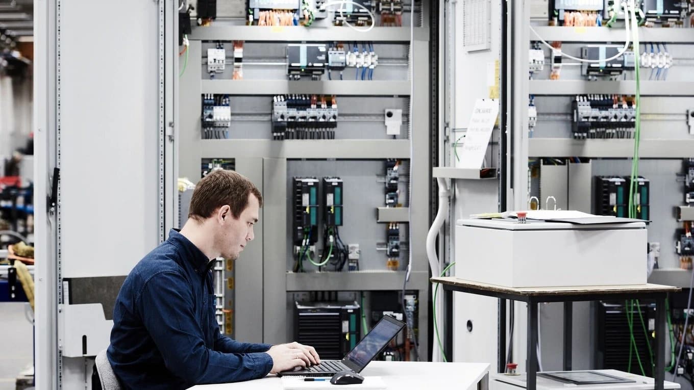 A factory worker operates a laptop, concentrating on cyber security within the supply chain.