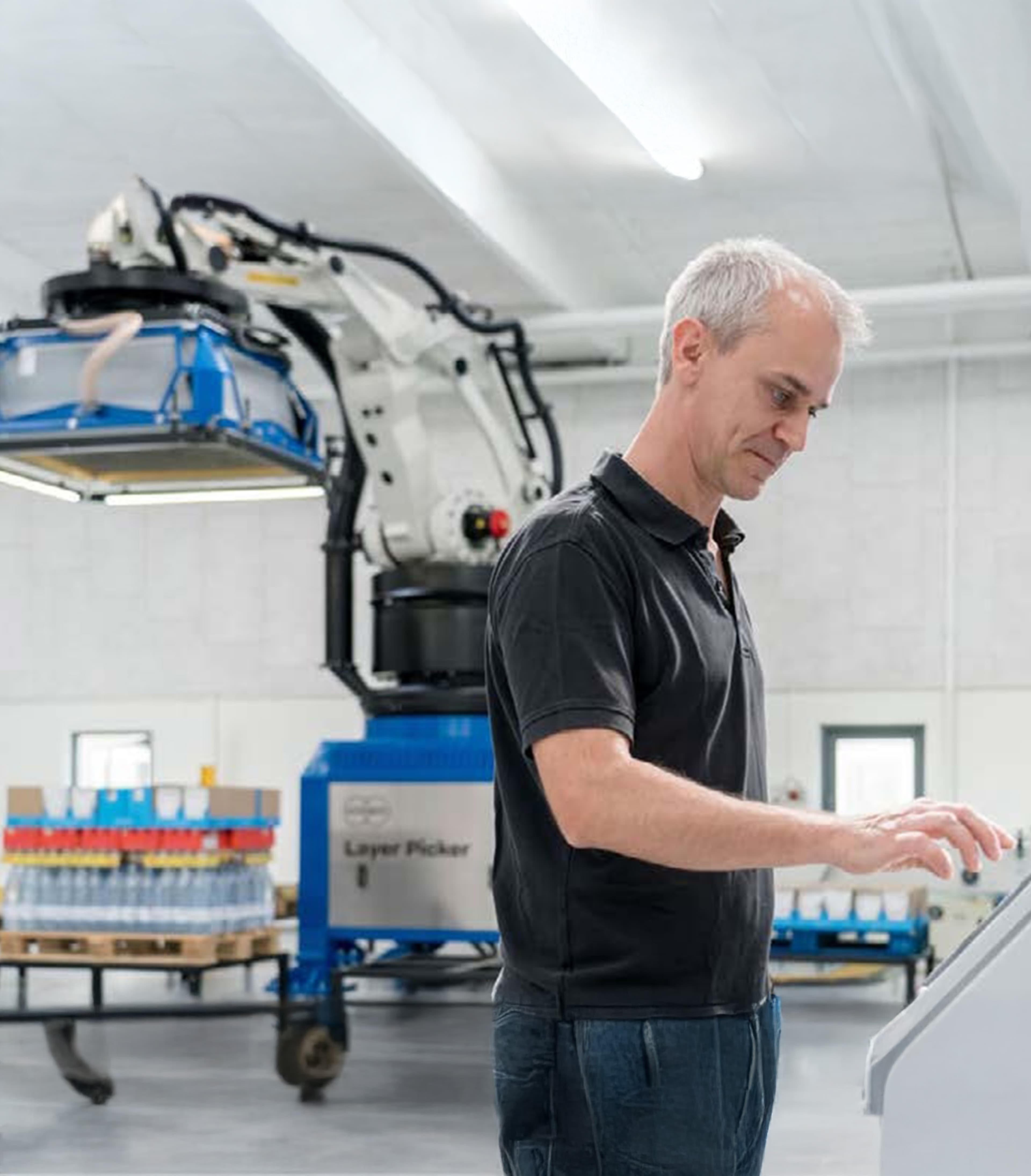 Ingenieur, der ein Bedienfeld vor einem Industrieroboterarm bedient, der verpackte Waren transportiert.