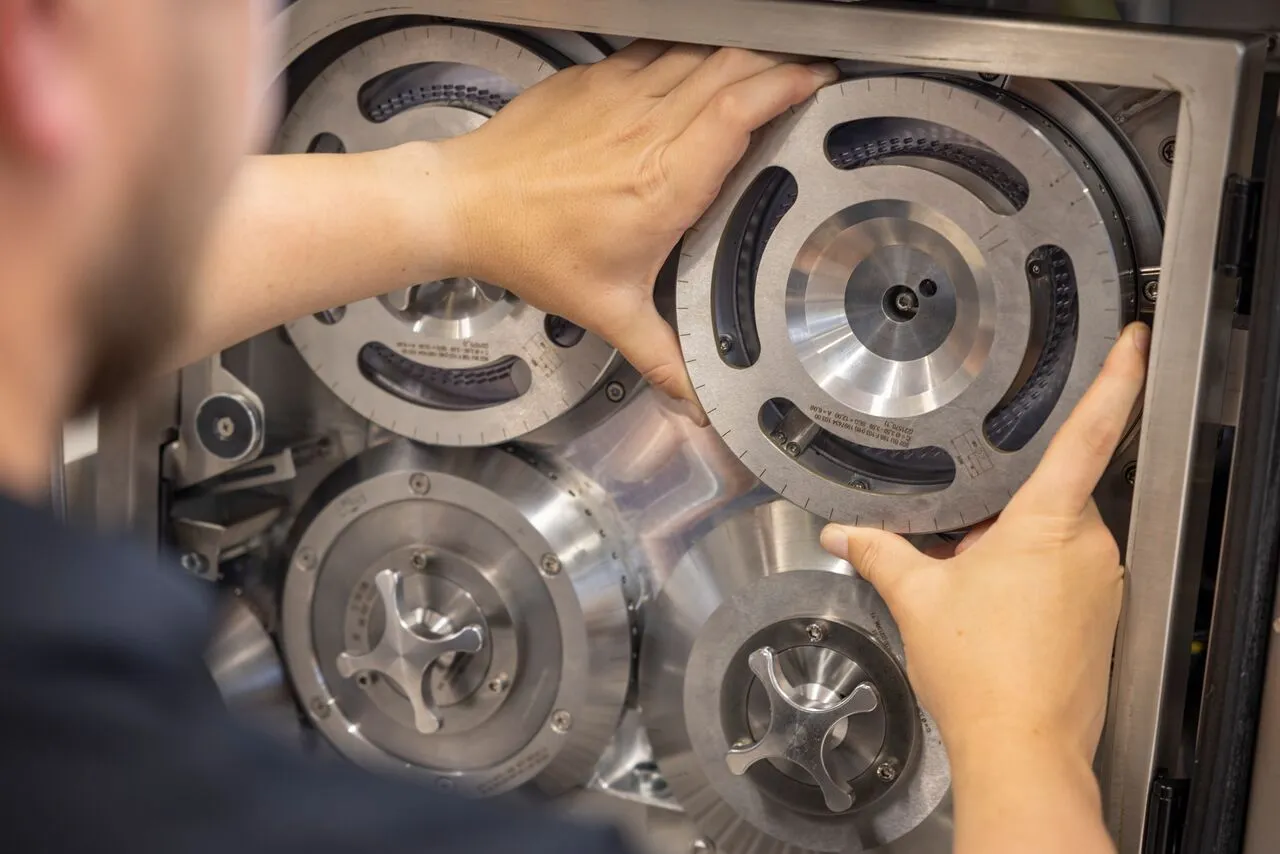 A man is carefully positioning a metal plate onto a machine