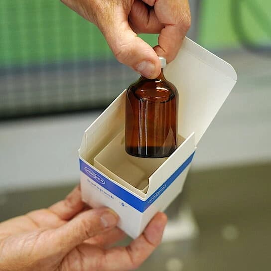 Closeup of a small medicine bottle inside a small package box. 
