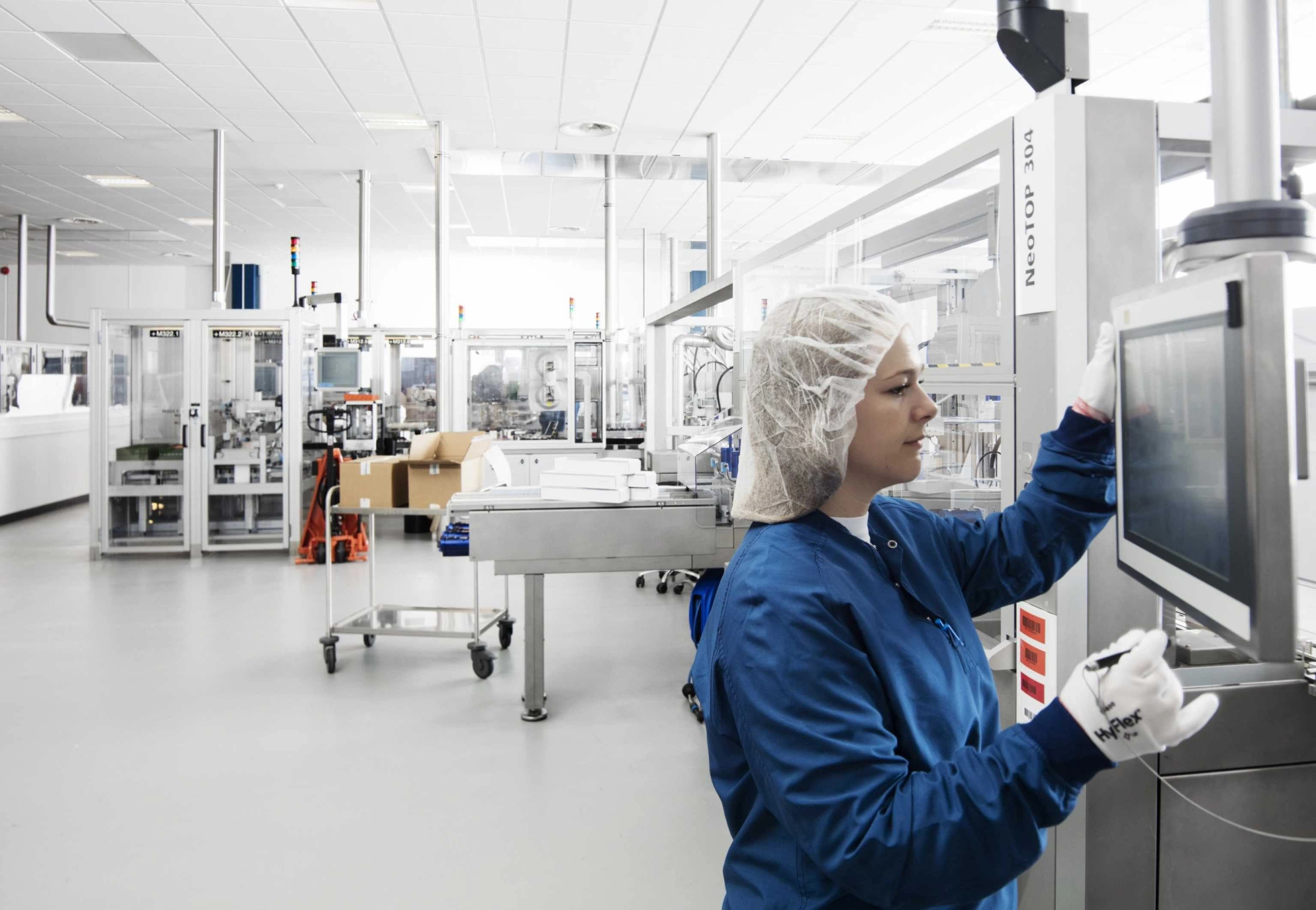 A woman in a factory is setting up a computer at a workstation, surrounded by machinery and equipment.