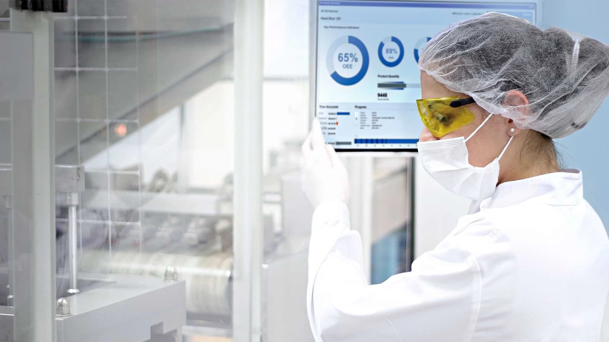 Frau in Laborkittel untersucht Daten auf einem Computerbildschirm im Labor.