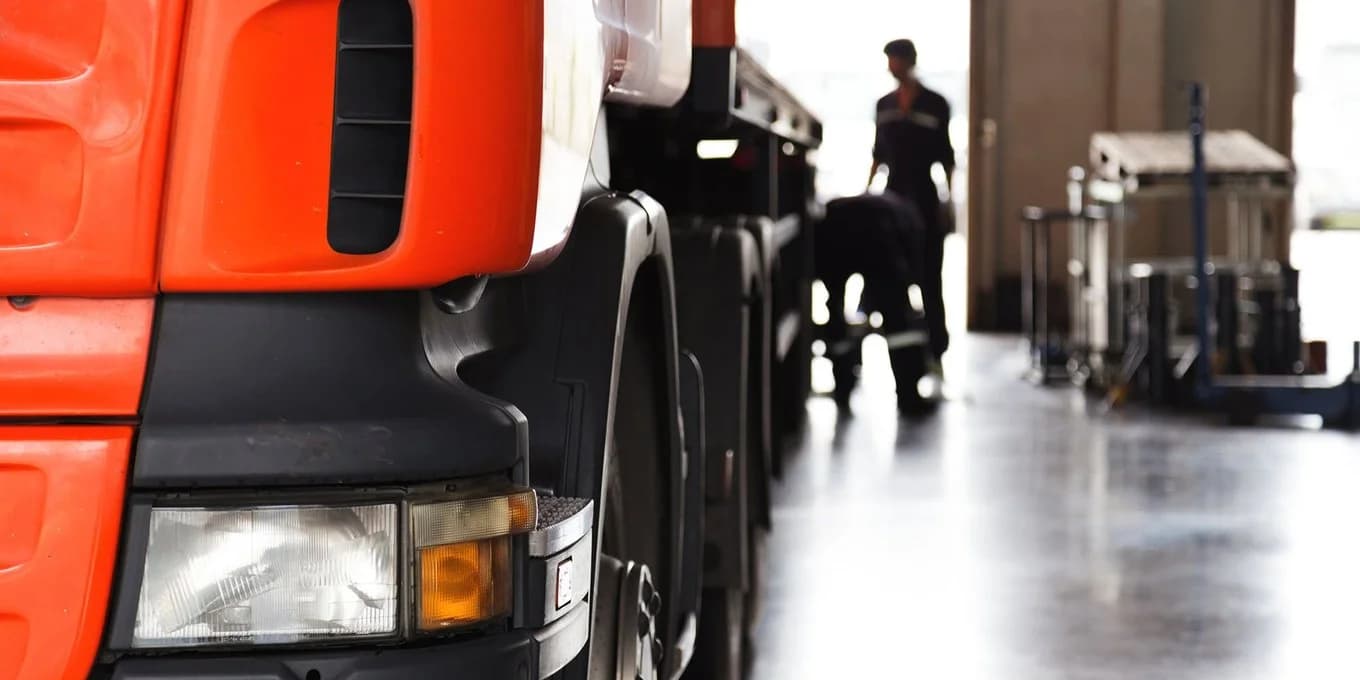 A man is next to a truck in a warehouse, illustrating a scene from the transport logistics sector.