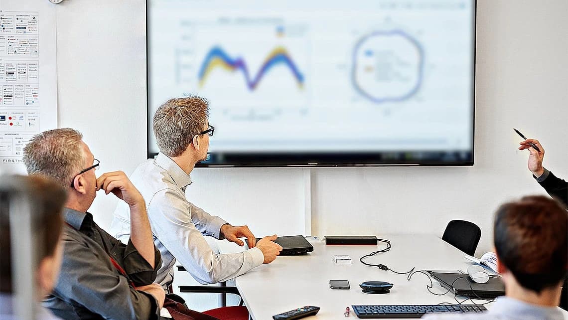 People gathered in a meeting room focused on sustainability, with a projector screen showing relevant data.
