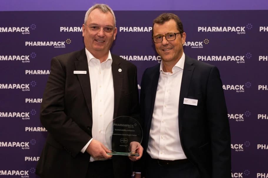 Two men in suits proudly hold a sustainability award for plastic-free COVID-19 tests at Pharmapack.