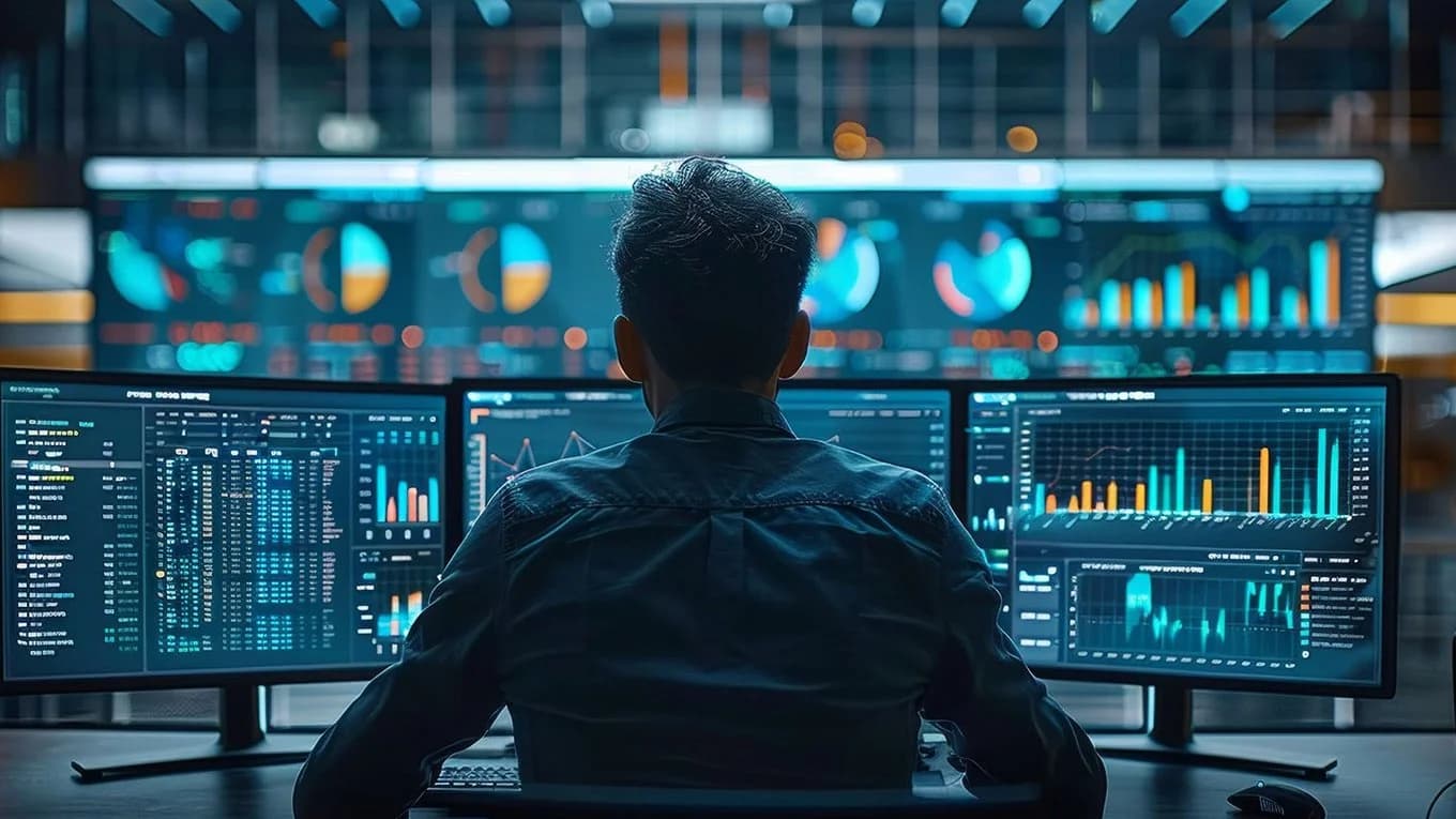 A man at a desk with three computer screens, working on projects involving SAP BTP.