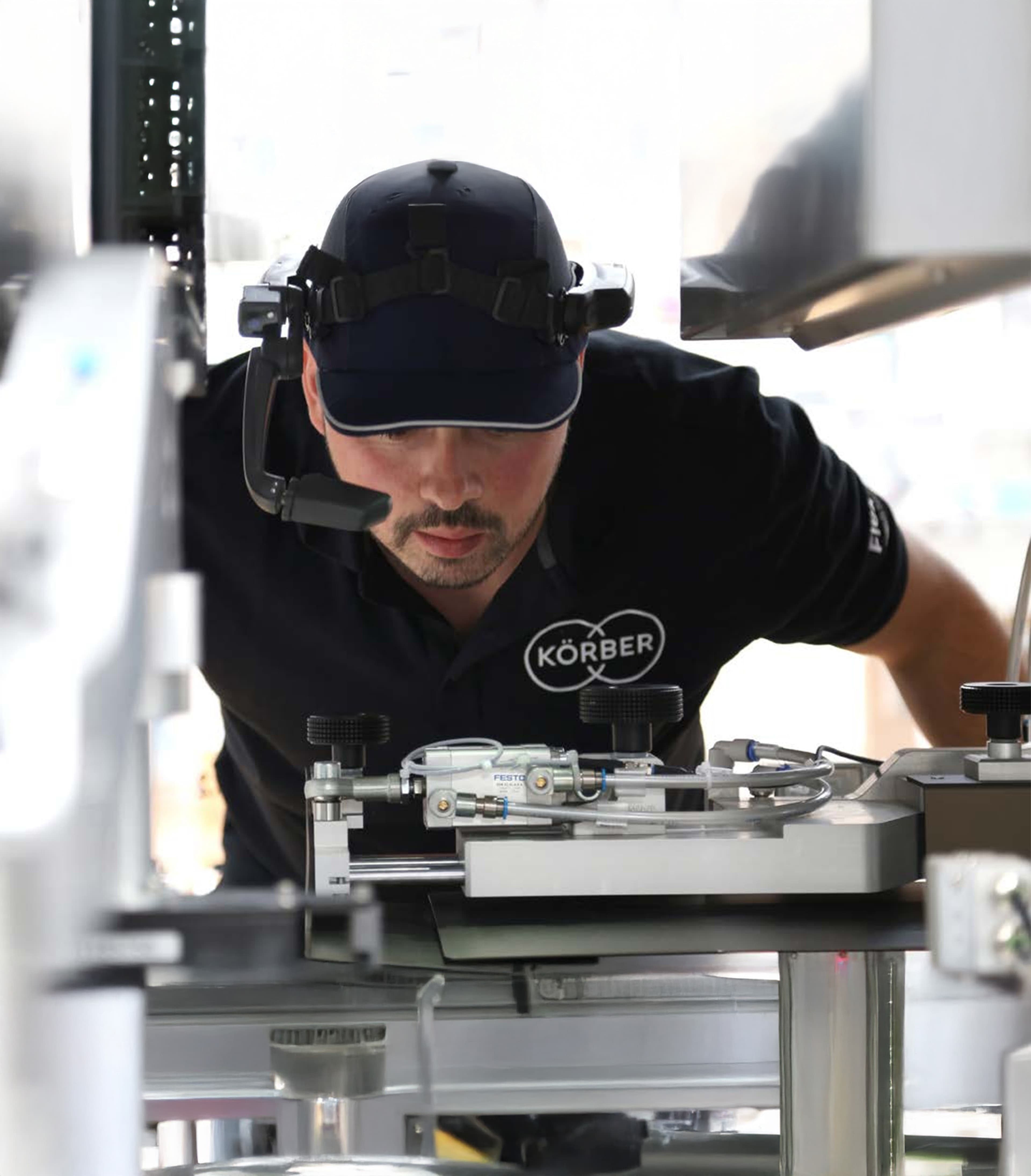 Ein Techniker mit Headset und Kappe inspiziert Industriemaschinen bei Körber.
