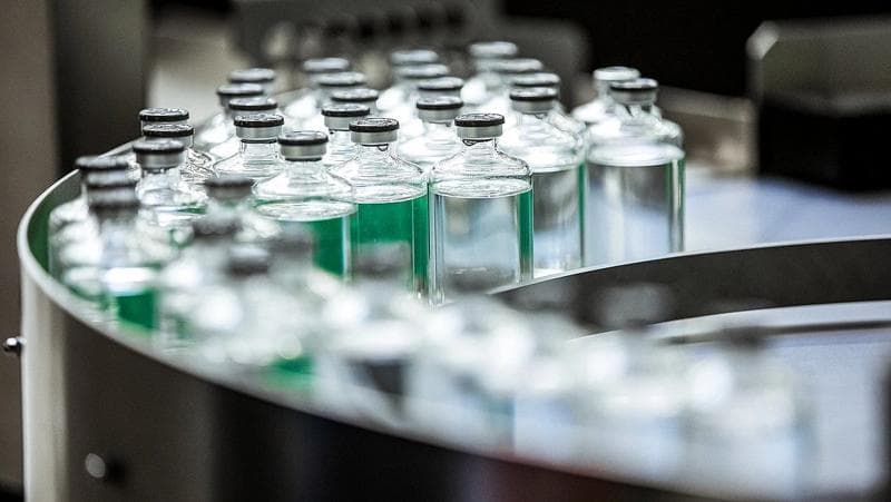 Eine Reihe von mit grüner Flüssigkeit gefüllten Flaschen, die die Inspektionsmaschinen von Körber Pharma für die Produktionssicherheit zeigen.