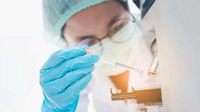 Person mit medizinischer Schutzausrüstung, die mit einer Pipette arbeitet.