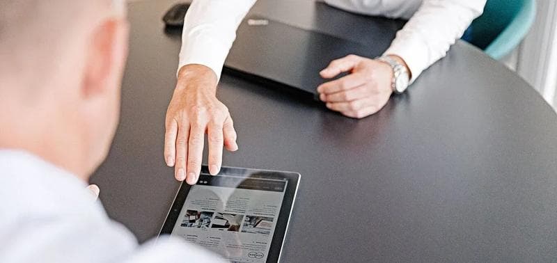 Two people around a desk with a tablet and computer.