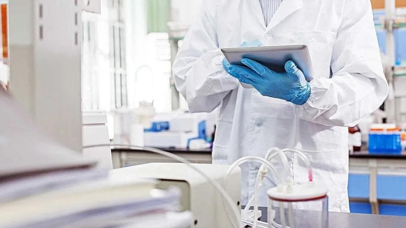 Person mit Tablet in Laborschutzkleidung.