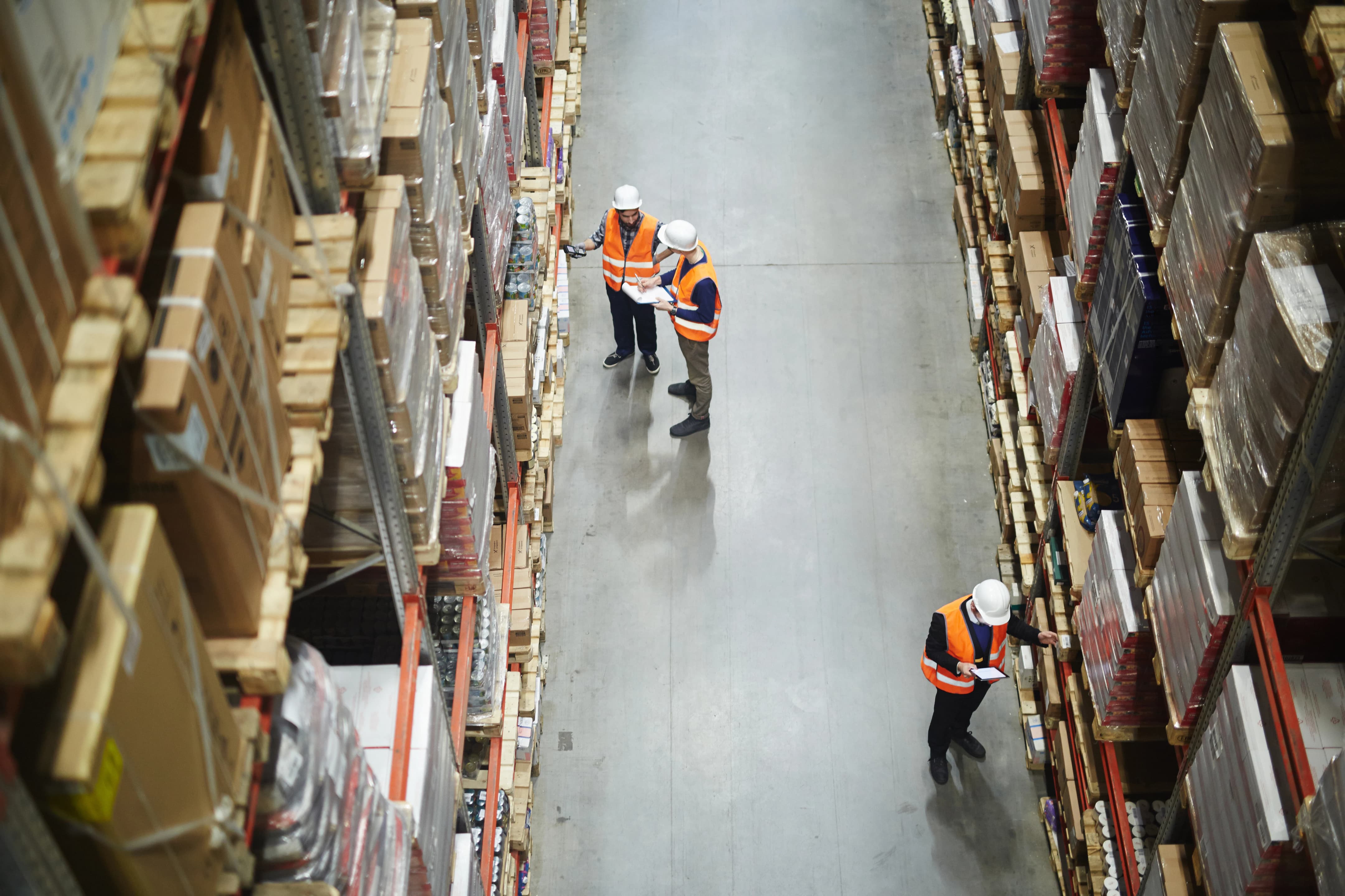Warehouse workers in safety vests checking inventory in a storage aisle.