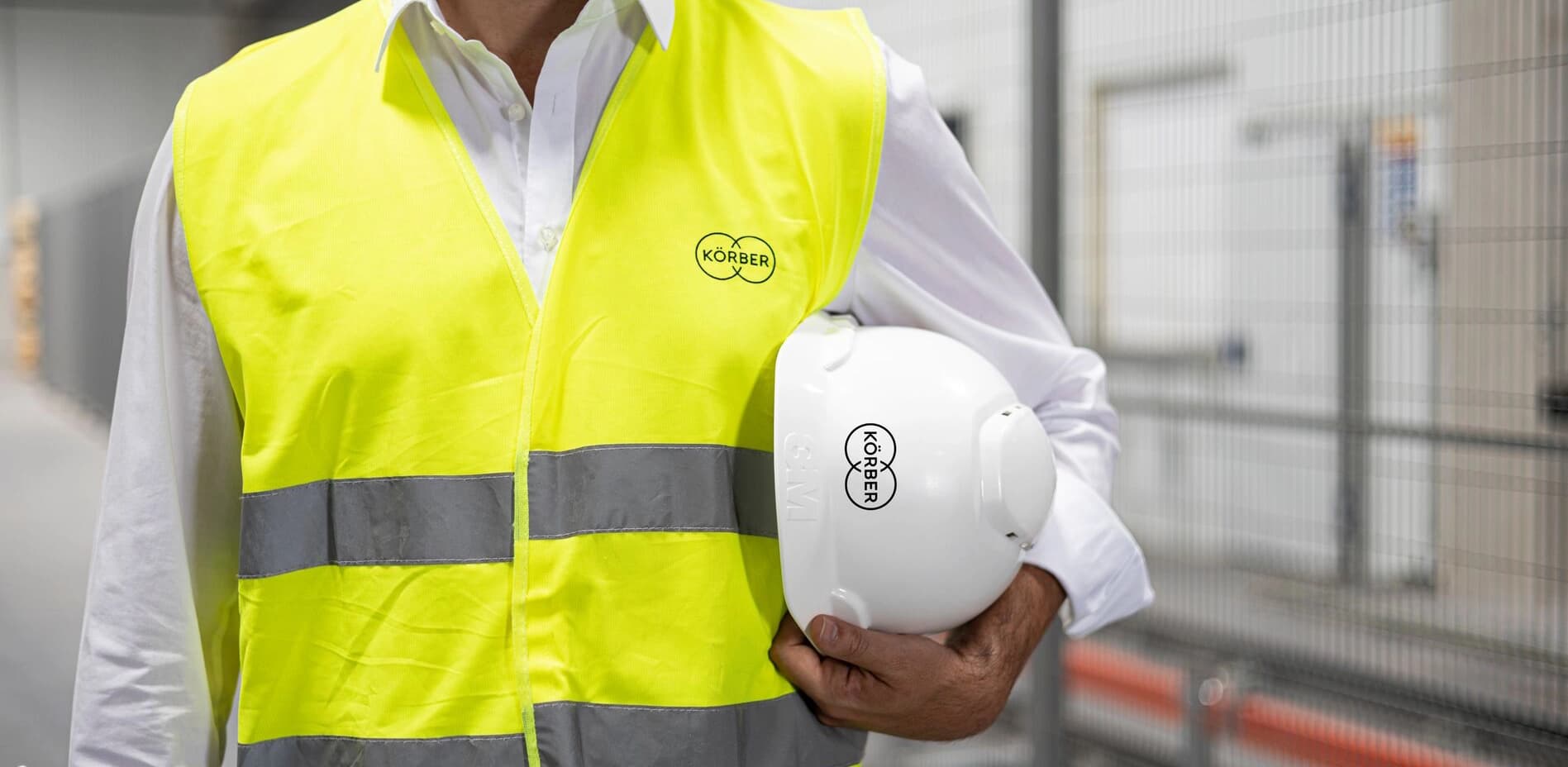 Employee with a yellow vest and a security hat with the Körber logo.
