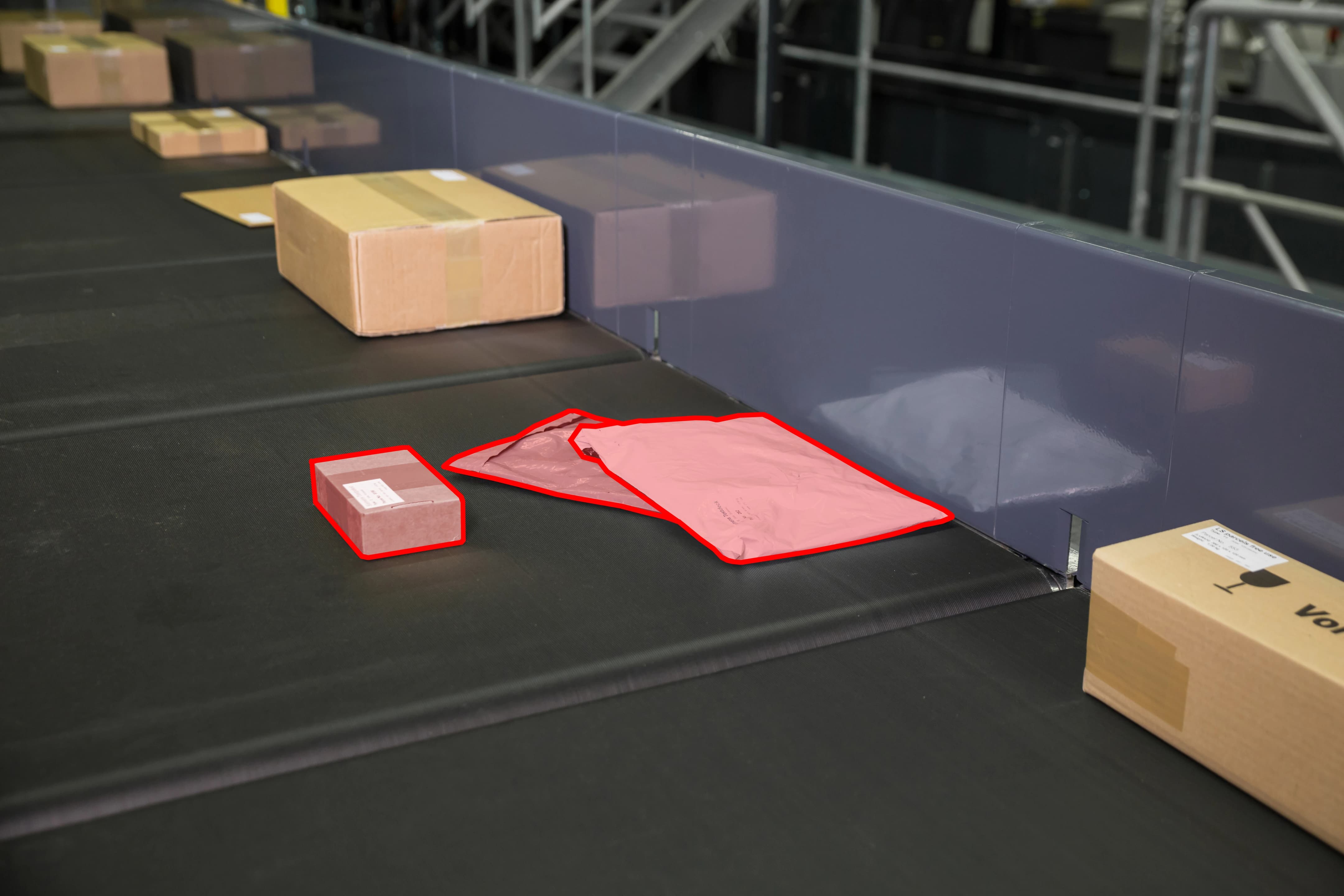 A parcel conveyor belt with cardboard boxes and two pink highlighted packages outlined in red.
