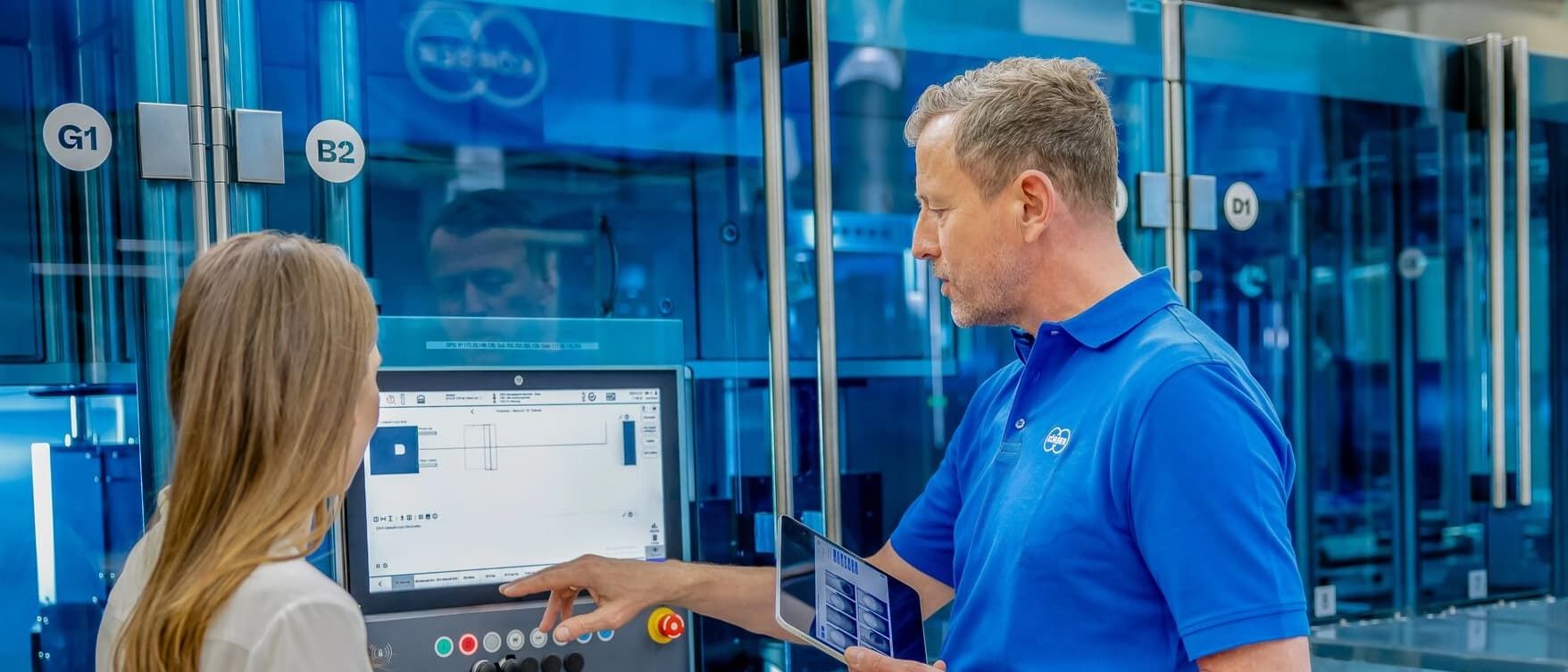 A man and woman in blue shirts are focused on a computer screen together.