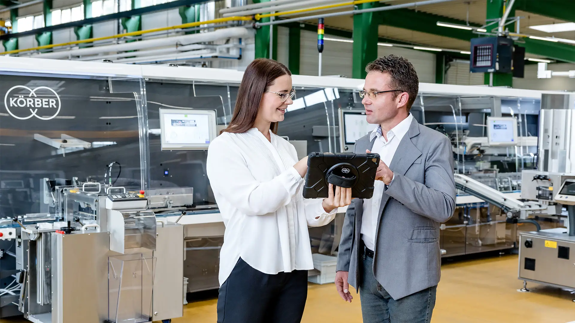 Two Körber employee discussing ideas with a tablet in a warehouse setting.