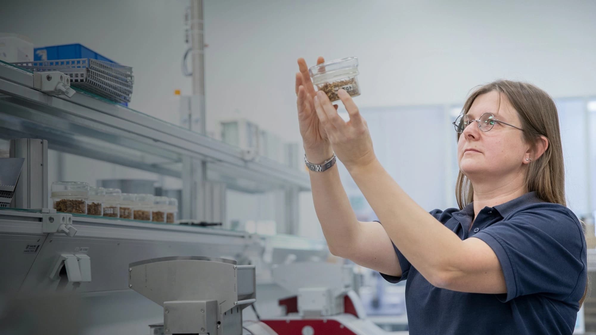 A woman in a lab environment raises a glass jar