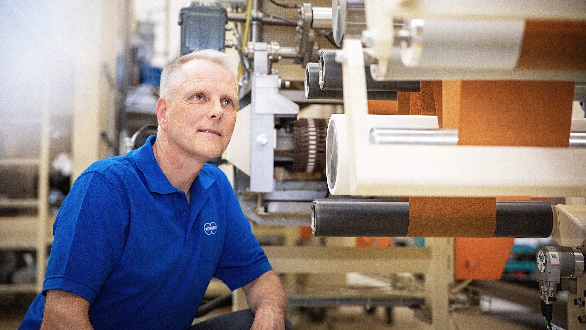 A Körber employee seated on a machine, focused on his task in a workshop environment.