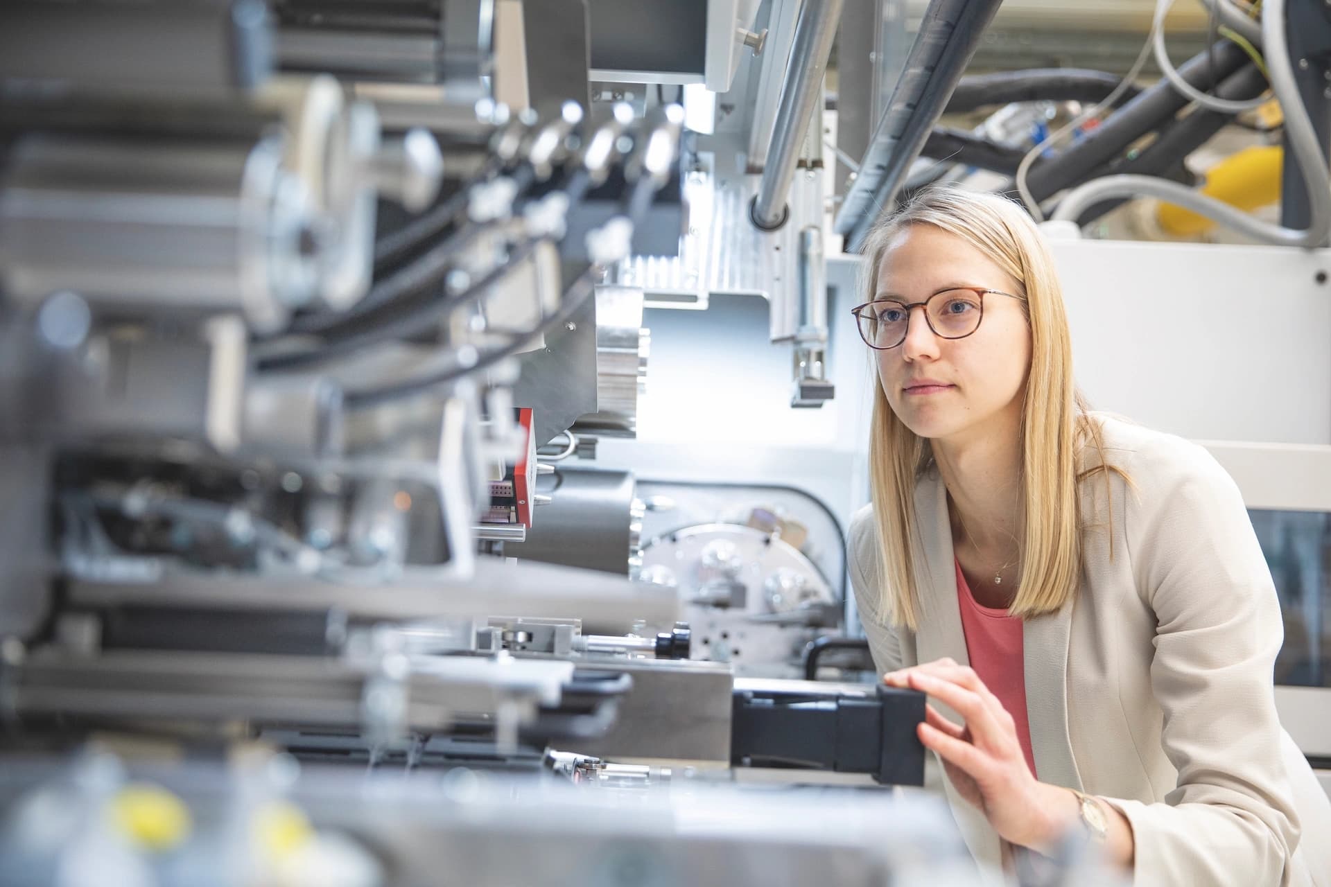 A woman with glasses is engaged in operating a machine, demonstrating concentration in a technical setting.