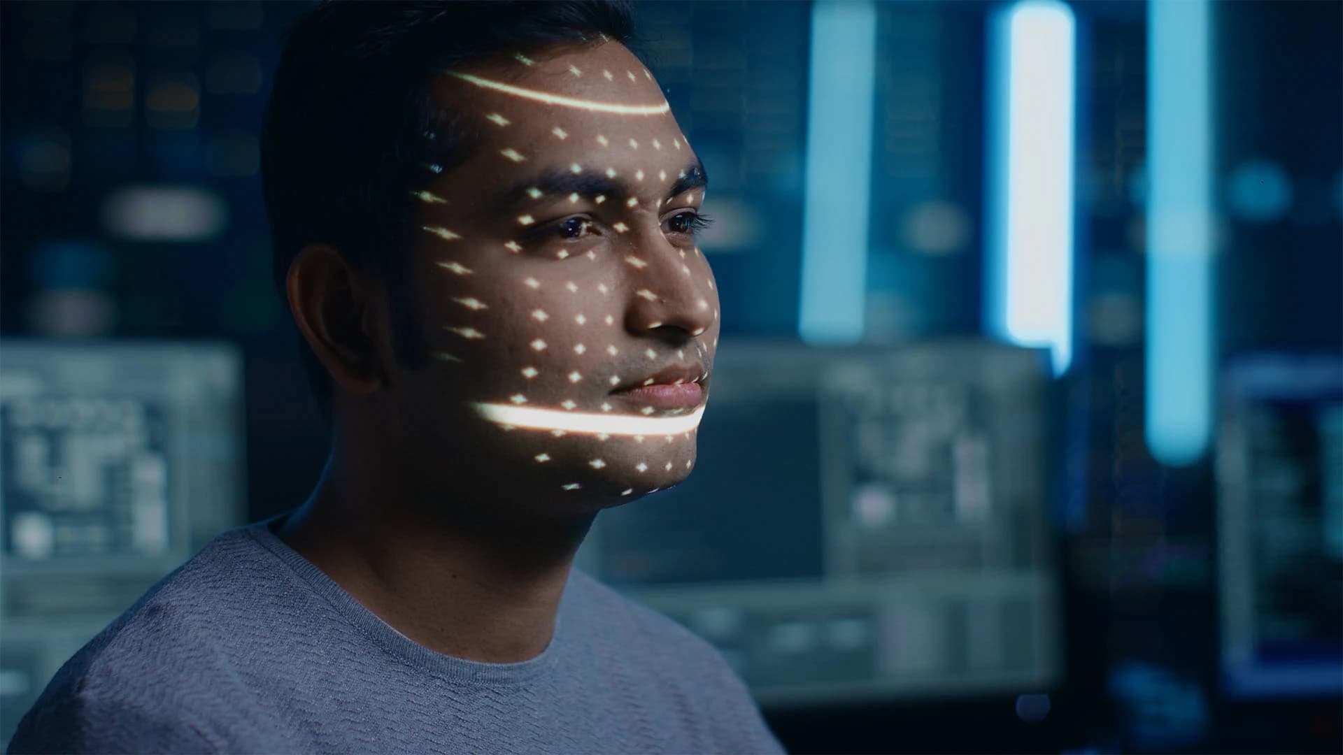 Person working in front of multiple computer screens in a blue-lit technology environment.